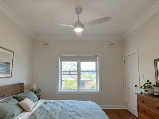 Ceiling fan in a bedroom with white walls, window, bed and timber furniture in Woy Woy