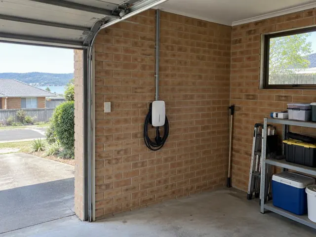 Wall-mounted EV charger on a brick garage wall beside the driveway in a suburban home in Umina Beach